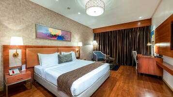 A hotel room with a large bed, a desk, a chair, and a painting on the wall.