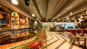 Zona de bar con una barra alargada, distintas opciones de asiento y una variedad de botellas en estanterías.