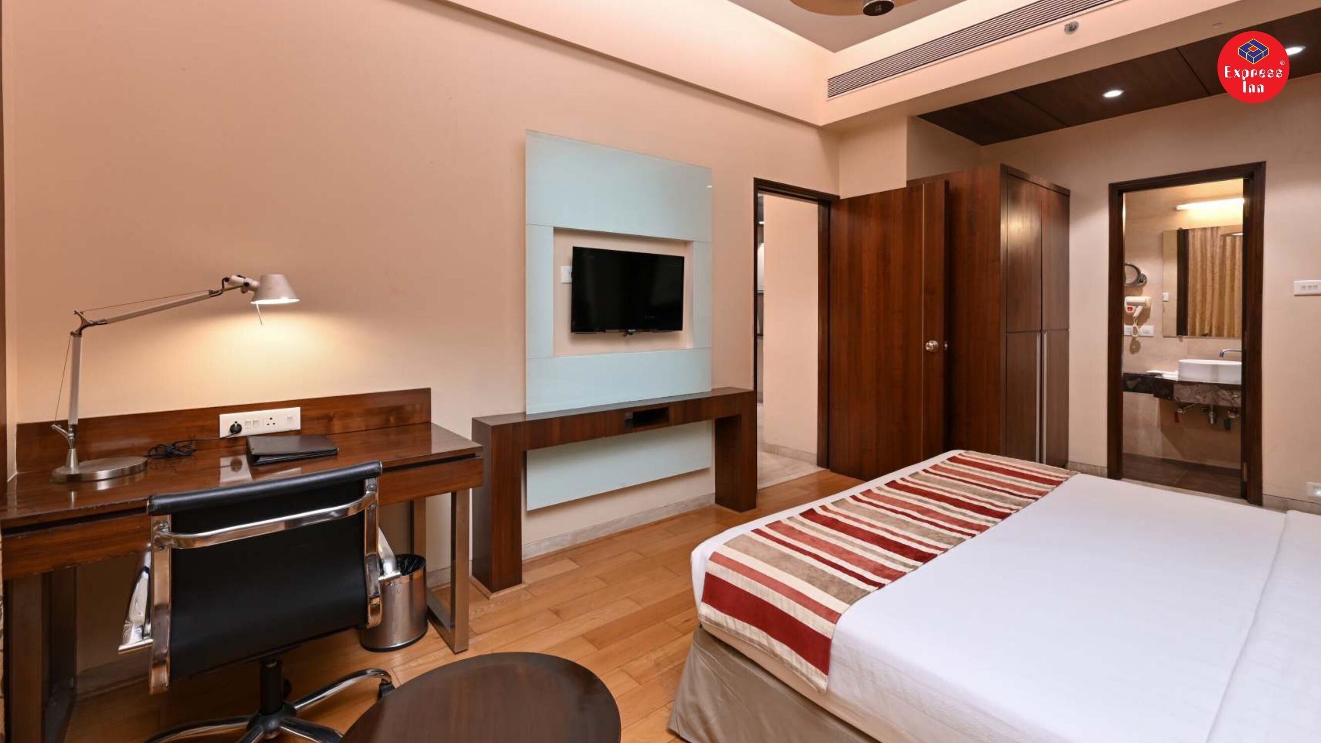 A hotel room with a desk, chair, TV, wardrobe, and bed.