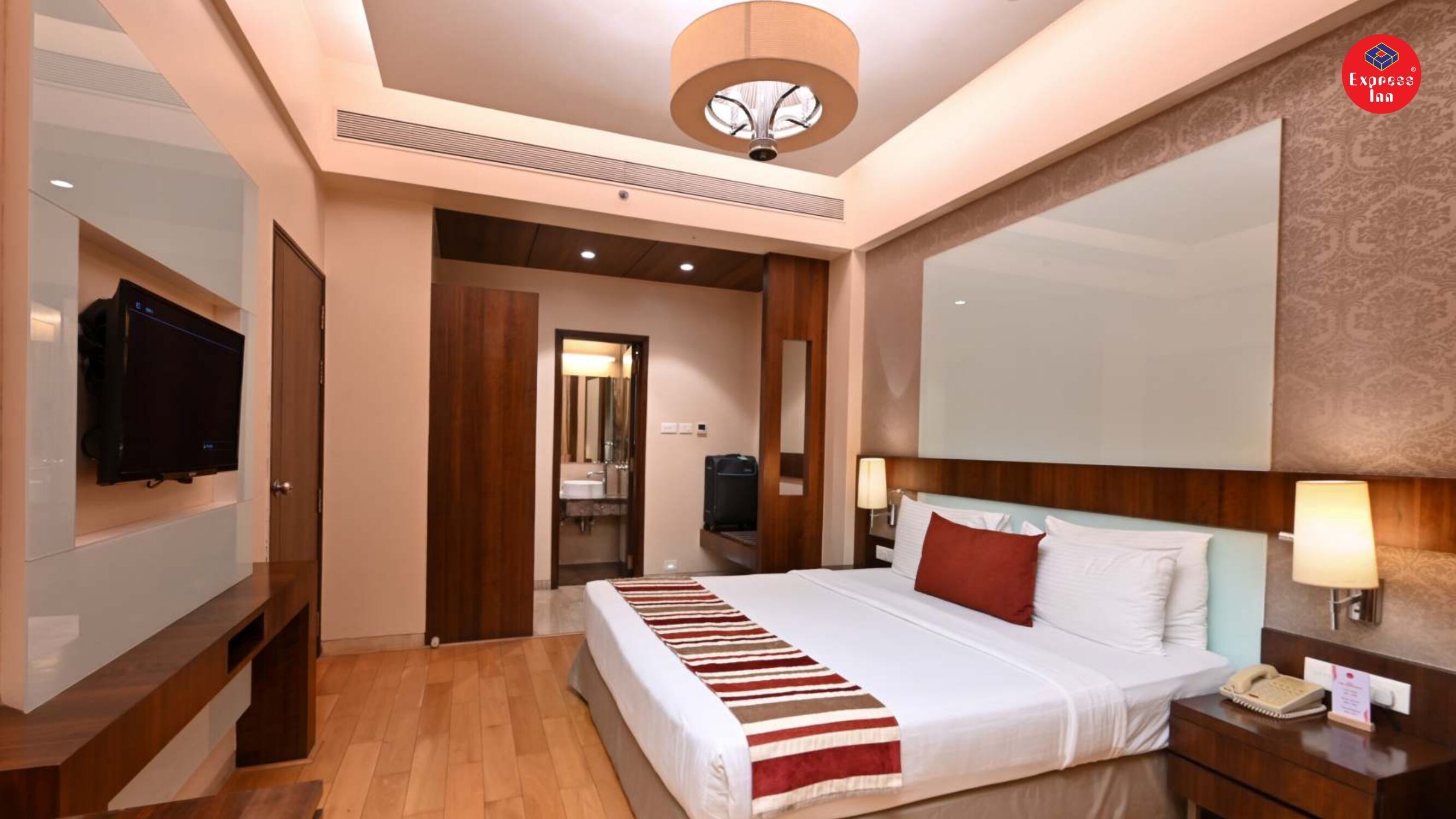 A hotel room with a bed, bedside tables, a TV, a mirror, and a ceiling light.