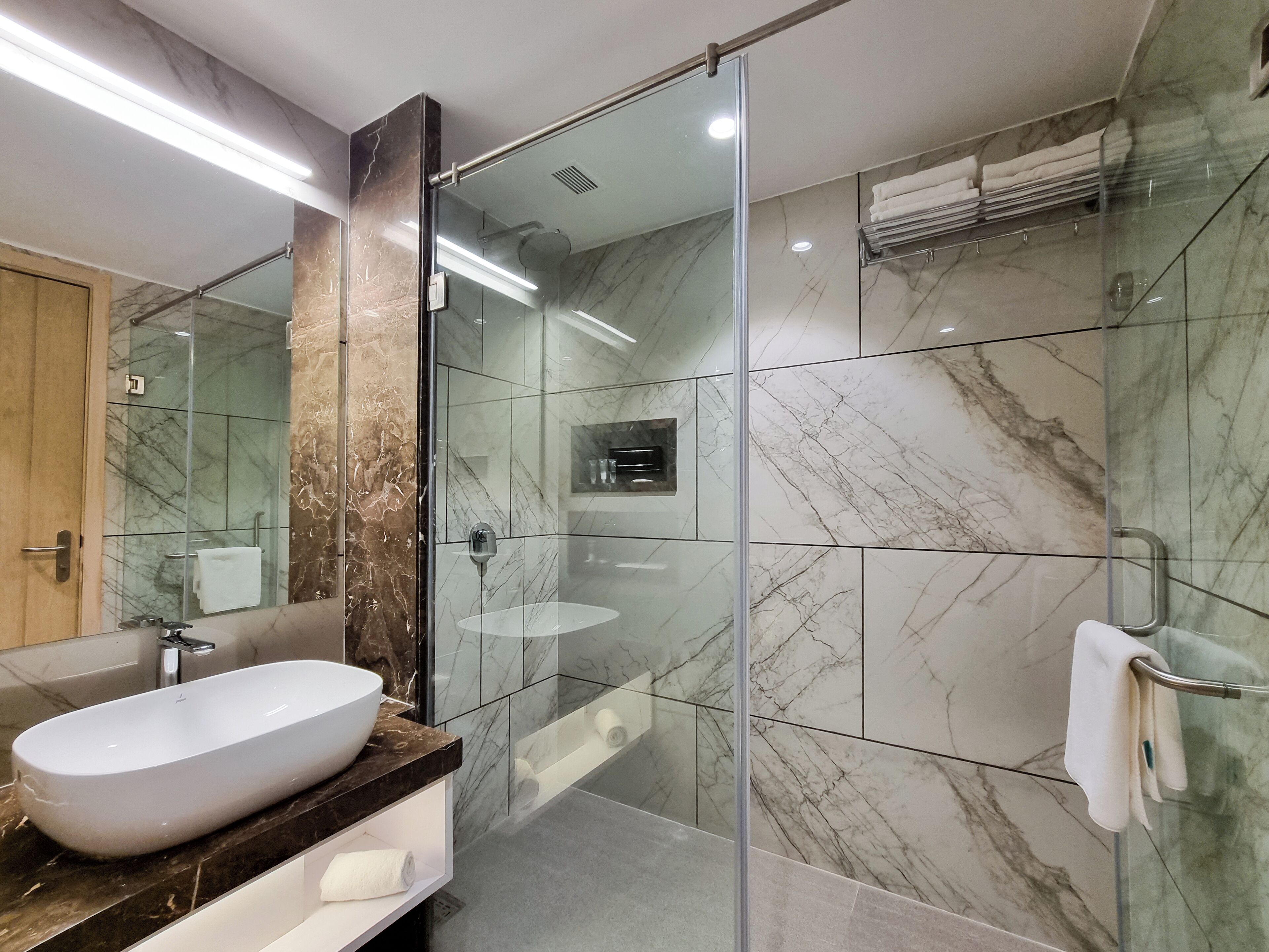 A modern bathroom with a glass-enclosed shower, a marble-tiled wall, and a large white sink.