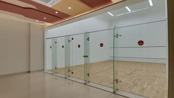 Een squashbaan met glazen wanden, houten vloer en plafondverlichting.