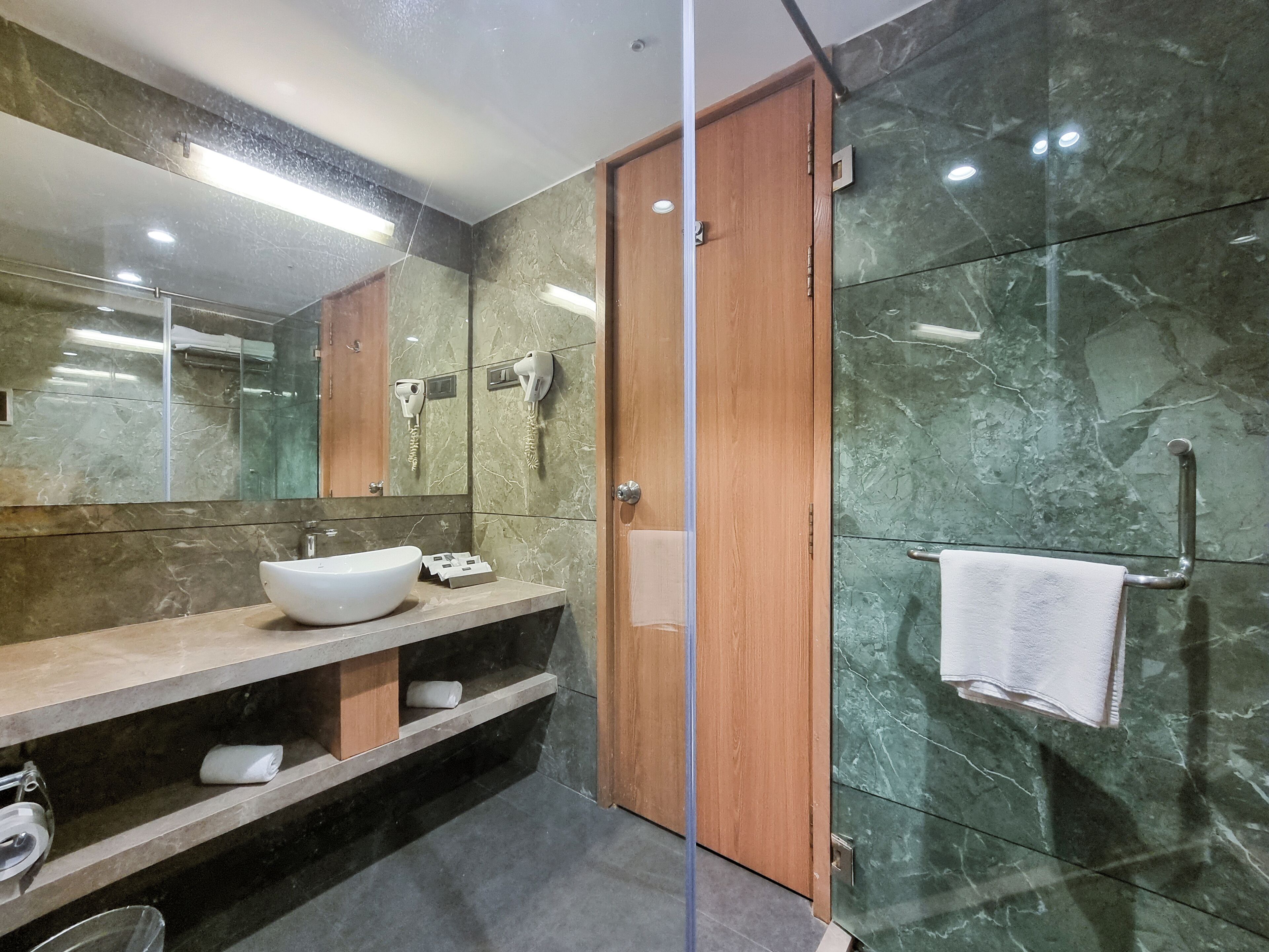 A modern bathroom with a large mirror, a white sink, a towel rack, and a glass shower enclosure.