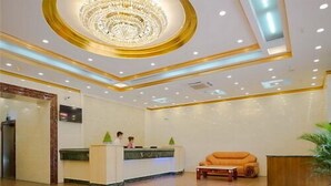 Un hall d’hôtel comprenant un comptoir d’accueil, un grand lustre et un motif décoratif sur le sol.