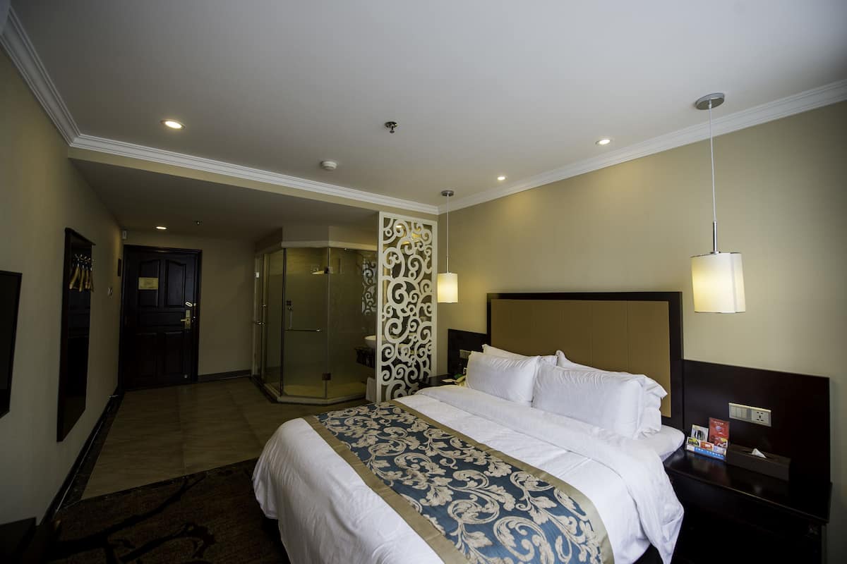 Een hotelkamer met een groot bed, een badkamer met douche en een deur naar een andere kamer.