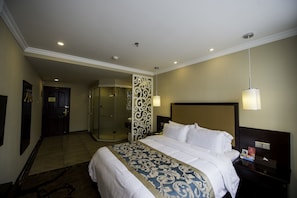 A hotel room with a large bed, a shower room, and a door leading to another room.