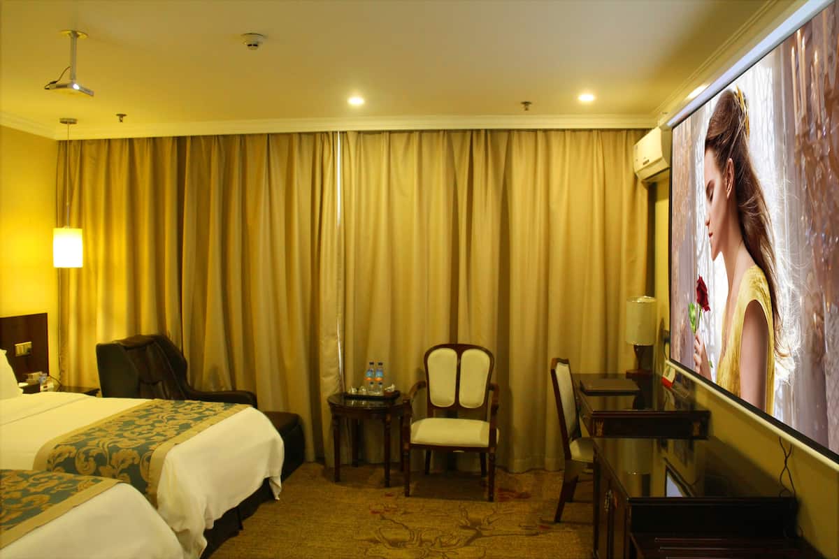 Een hotelkamer met twee bedden, een bureau, een stoel, een televisie en een gordijn.