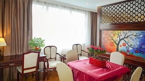 Un coin repas avec une table dressée pour quatre personnes, entourée de chaises, d’un tableau décoratif et d’une fenêtre agrémentée de rideaux.
