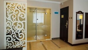 Une chambre d’hôtel avec une porte d’entrée en verre, un panneau décoratif blanc, une porte en bois foncé et un miroir agrémenté d’un luminaire.