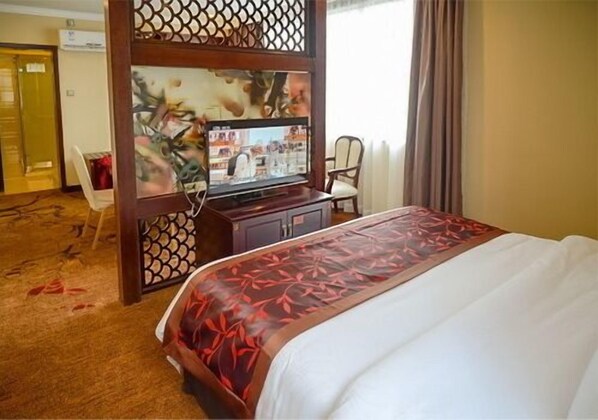 Quarto de hotel com cama, televisão, escrivaninha e cadeira.