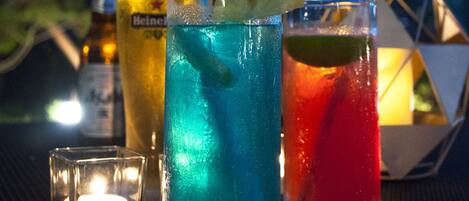 Tres vasos de bebidas sobre una mesa, con una botella y una vela al fondo.