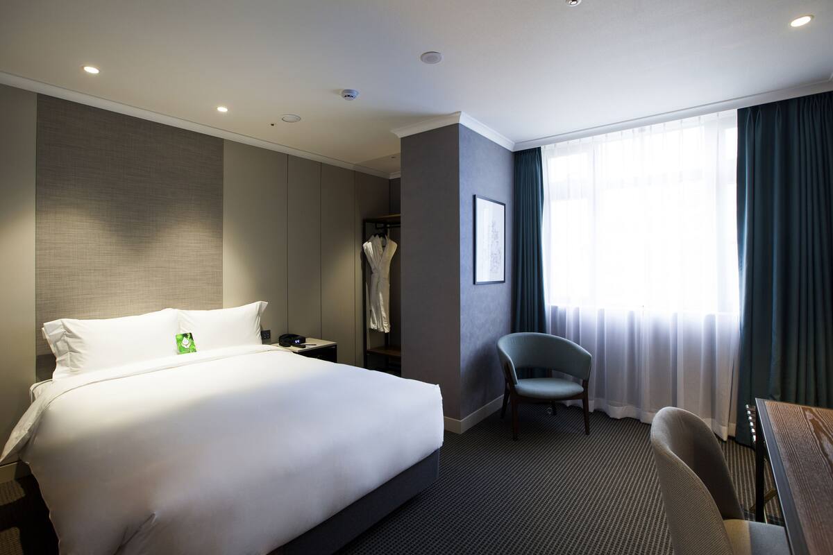 A hotel room with a large bed, a desk, a chair, a wardrobe, and a window with curtains.