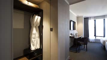 Habitación de hotel con vestidor, un escritorio con silla, cama y un gran ventanal con cortinas.