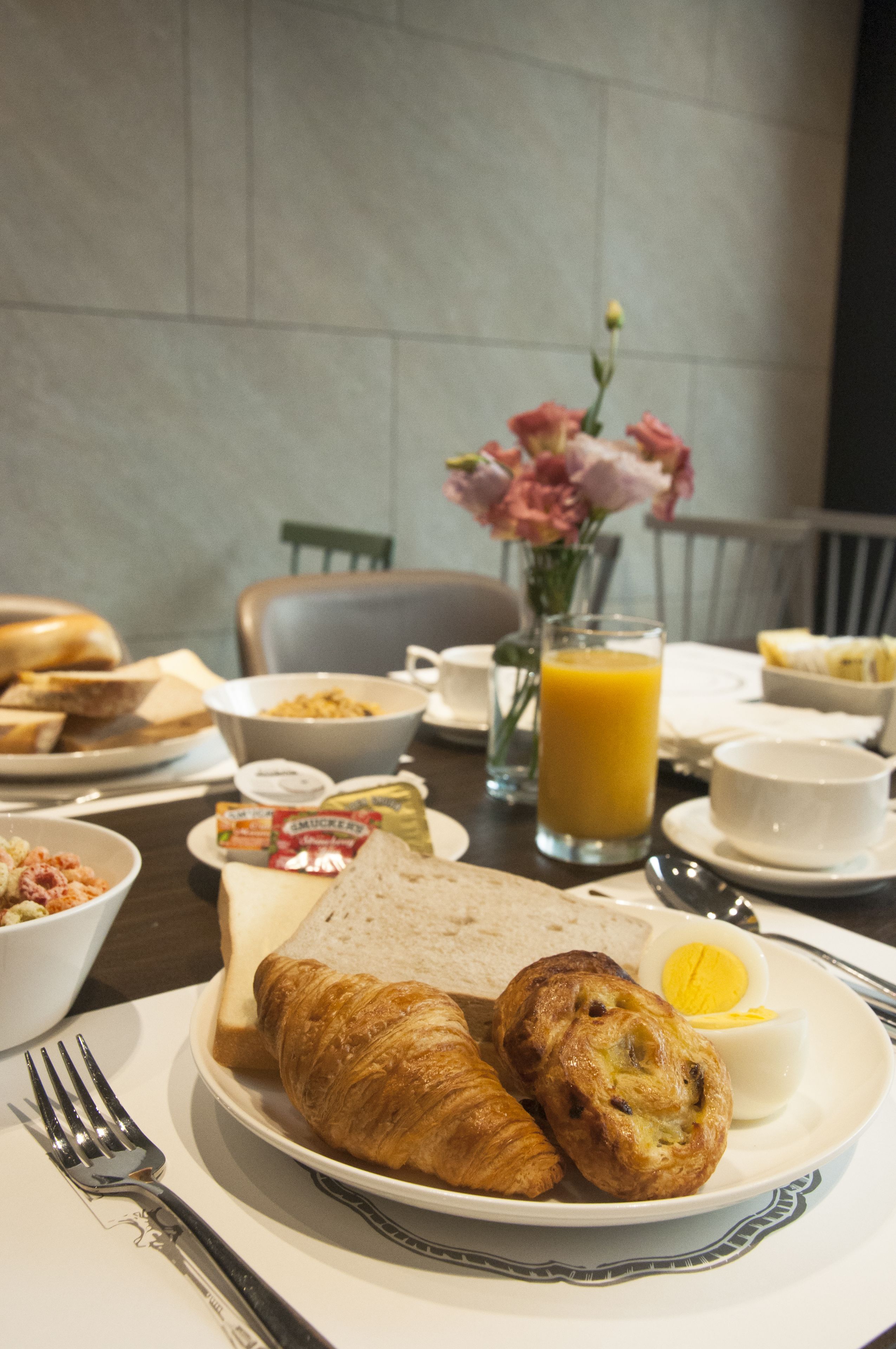 A breakfast setting with croissants, a glass of orange juice, and a vase of flowers on a table.