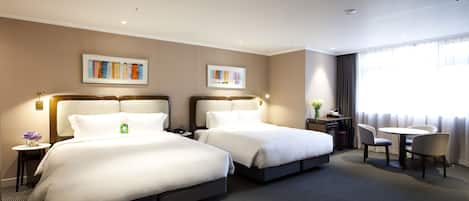 A hotel room with two beds, a desk, a chair, and a window with curtains.