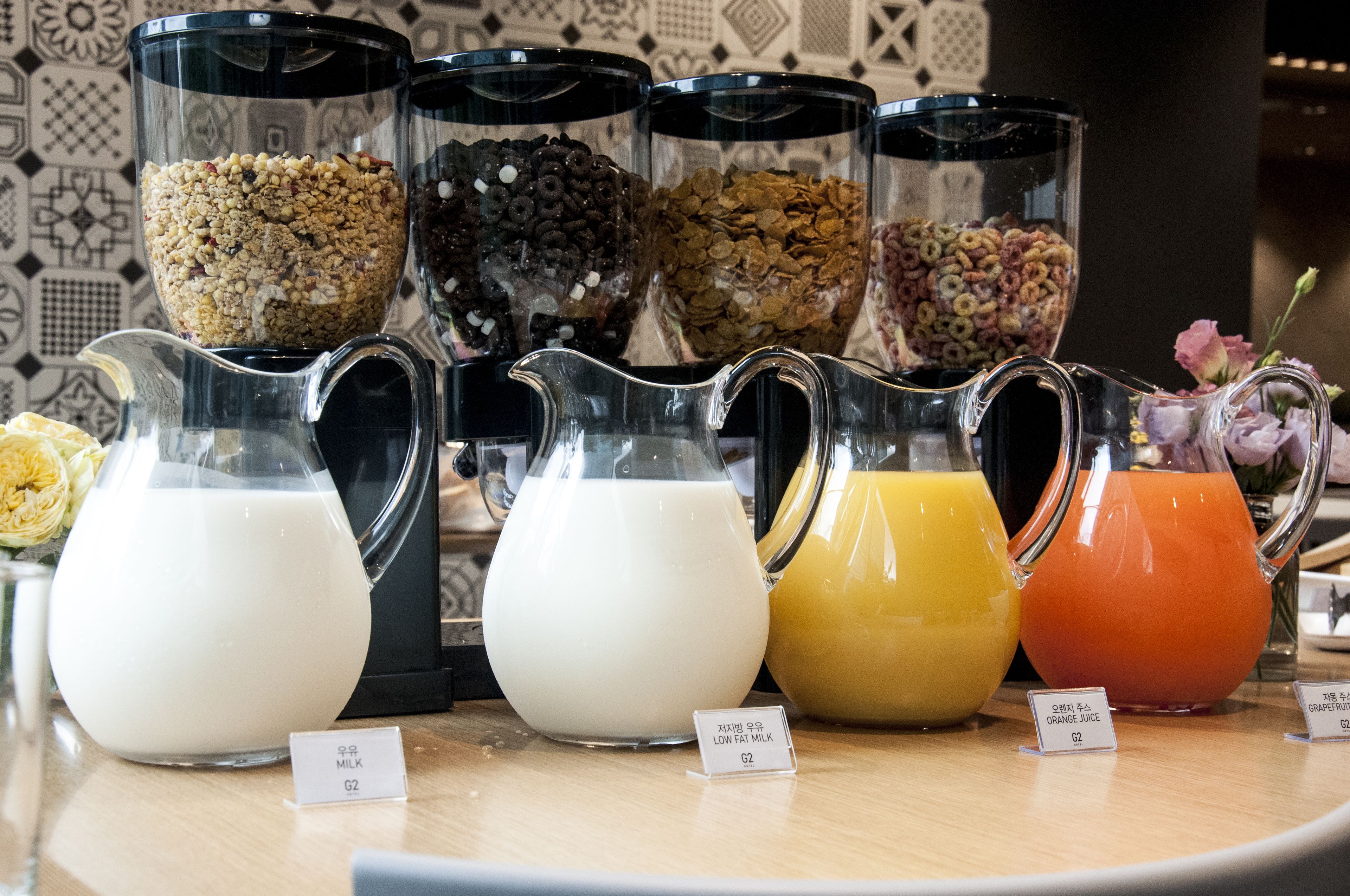 A breakfast bar with various food and drink options, including cereal, milk, and orange juice.