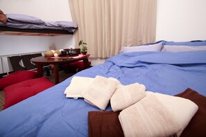 Ein Hotelzimmer mit einem Etagenbett, einem runden Tisch mit einer Pflanze und einer blauen Tagesdecke.