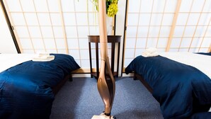 A room with two beds, a standing heater, and a small table with a vase of flowers. - Place Iine (Tokyo)