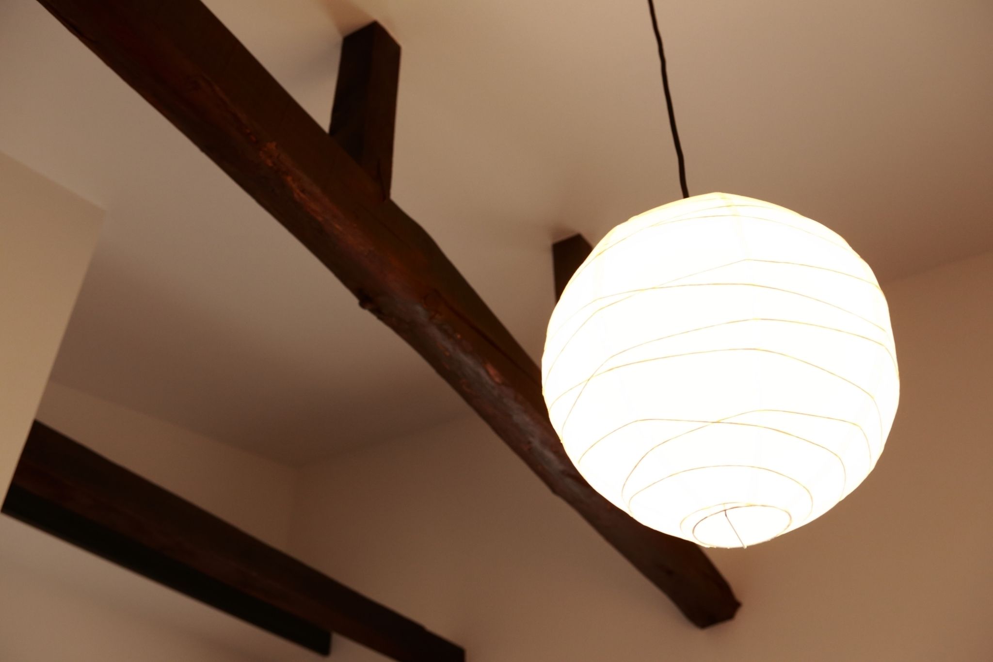 Un plafond avec des poutres en bois apparentes et un luminaire sphérique suspendu.