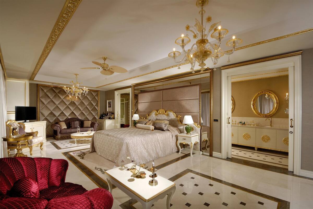 A luxurious bedroom with a large bed, a chandelier, a television, and a red sofa.