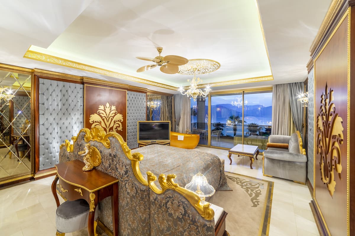A luxurious bedroom with a large bed, a television, a sofa, and a balcony with a view.