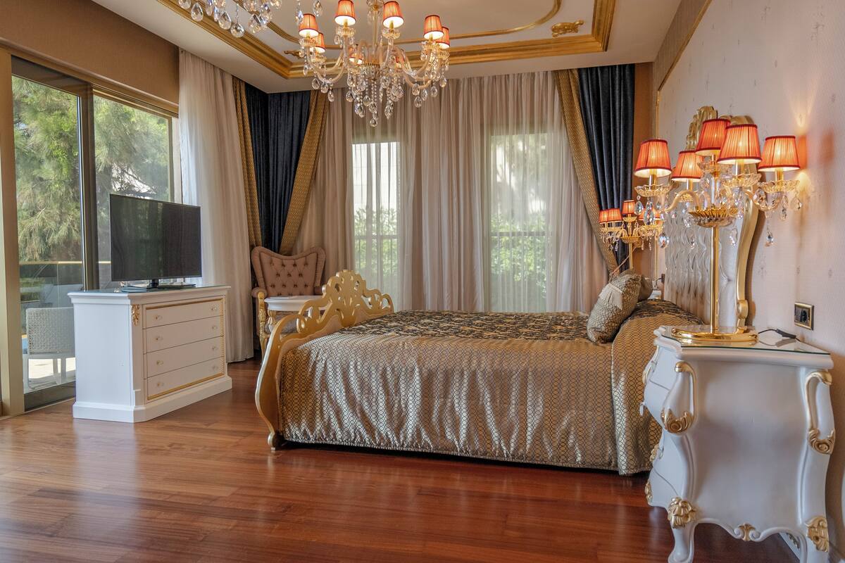 A luxurious bedroom with a large bed, a television, a white dresser, and a chandelier.
