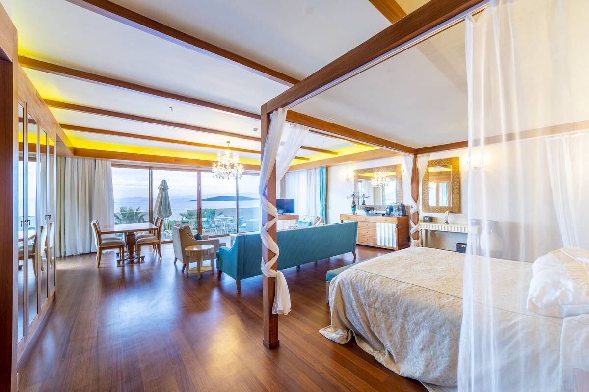 A spacious hotel room with a large bed, a balcony with a view, a dining area, and a bathroom.