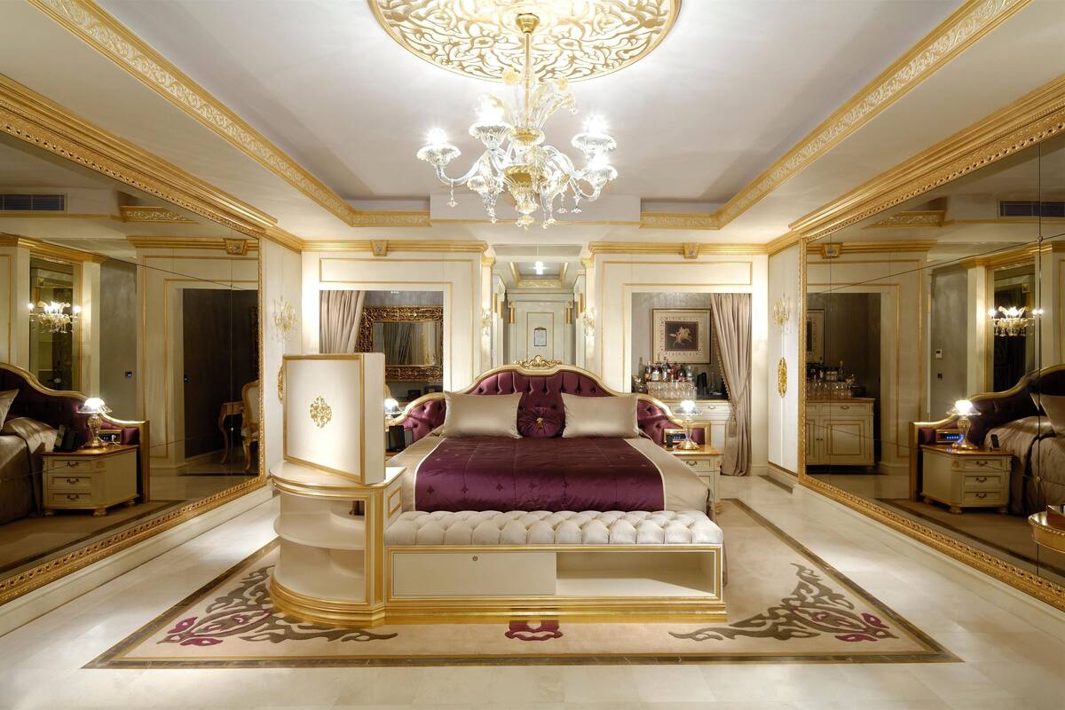 A luxurious bedroom with a large bed, ornate ceiling chandelier, and mirrored walls.
