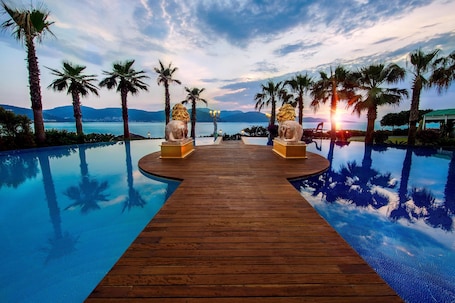 A wooden infinity pool with palm trees and a sunset view.