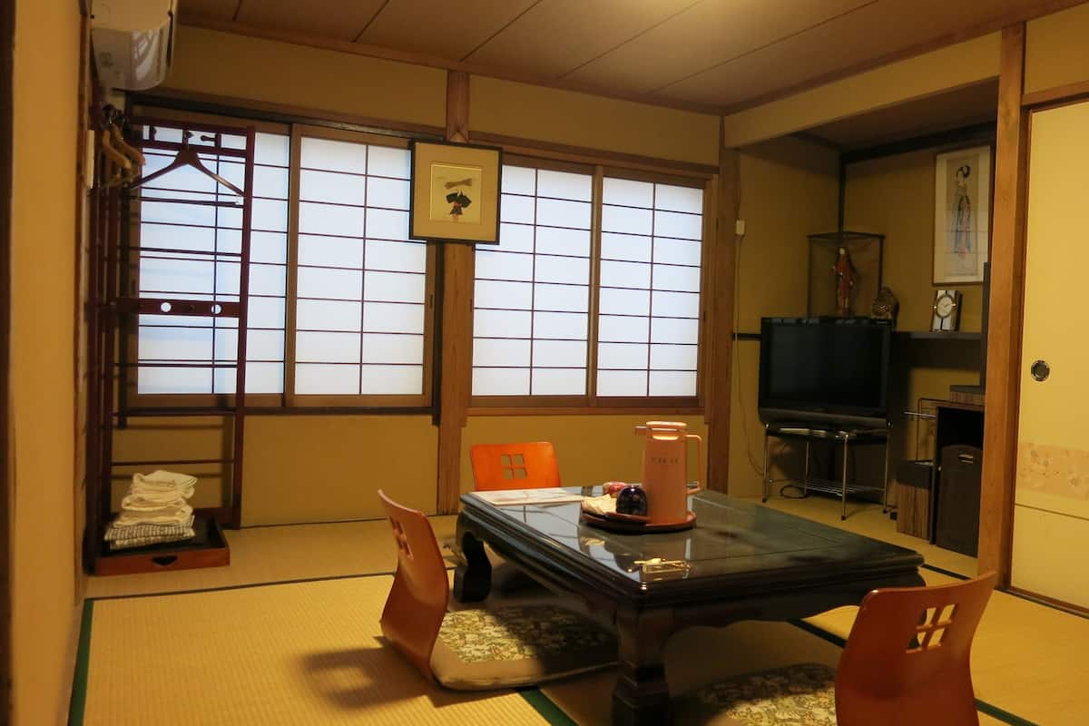 Una habitación japonesa tradicional con suelo de tatami, una mesa baja, dos sillas, un televisor y una puerta corredera.