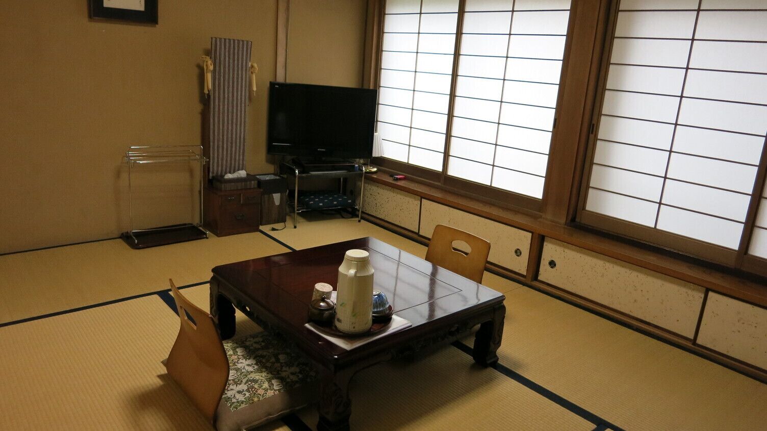Una habitación japonesa tradicional con suelo de tatami, una mesa baja con una tetera, un televisor y puertas correderas.