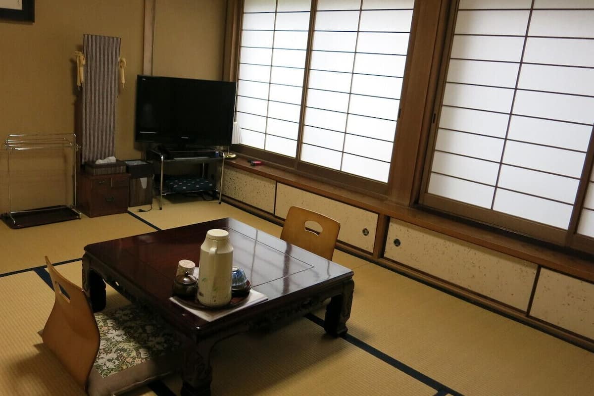 Una habitación japonesa tradicional con suelo de tatami, una mesa baja con una tetera, un televisor y puertas correderas.