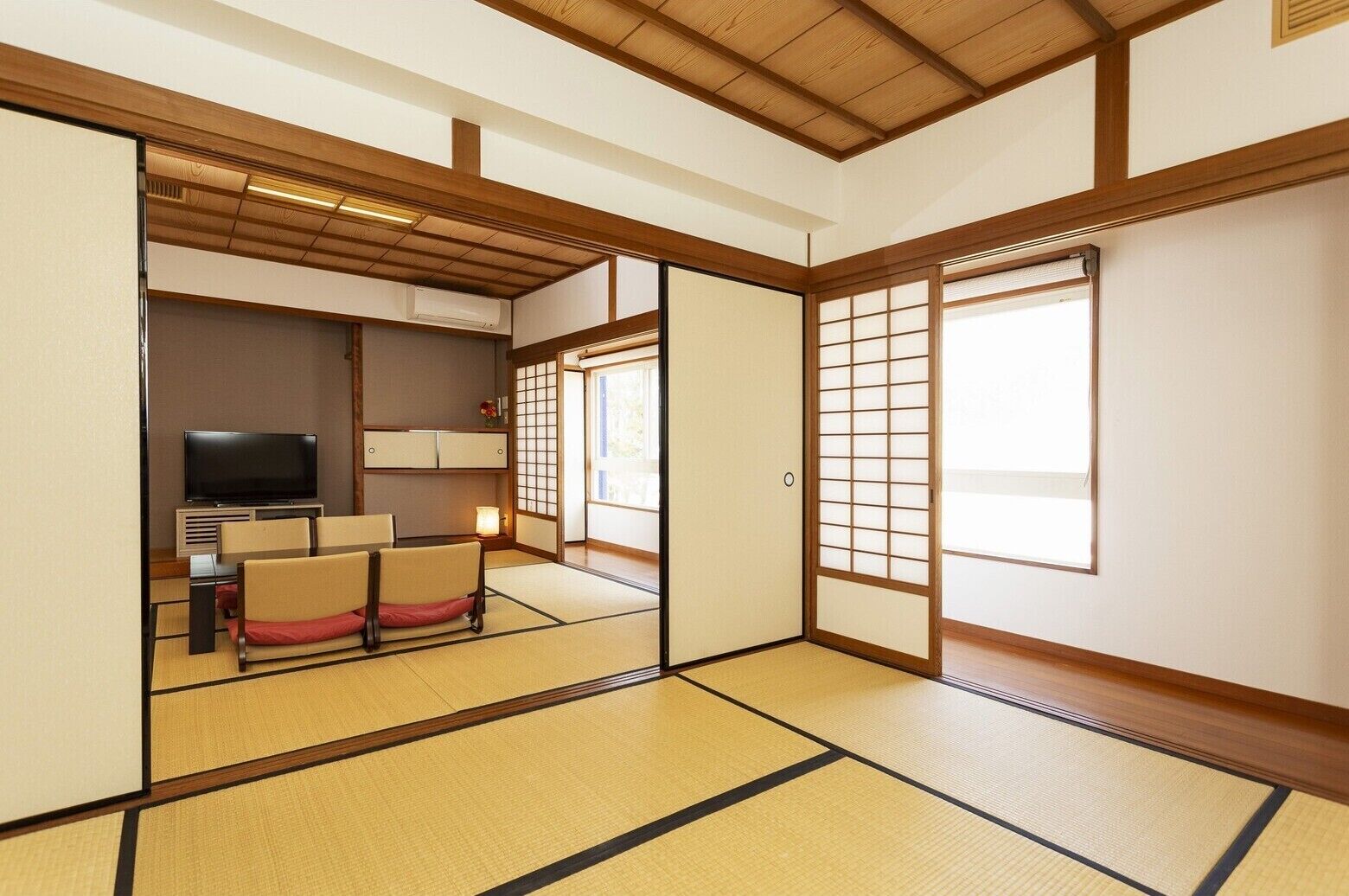 Ett traditionellt japanskt rum med tatamimattor på golvet, en tv, ett lågt bord med stolar och skjutdörrar.