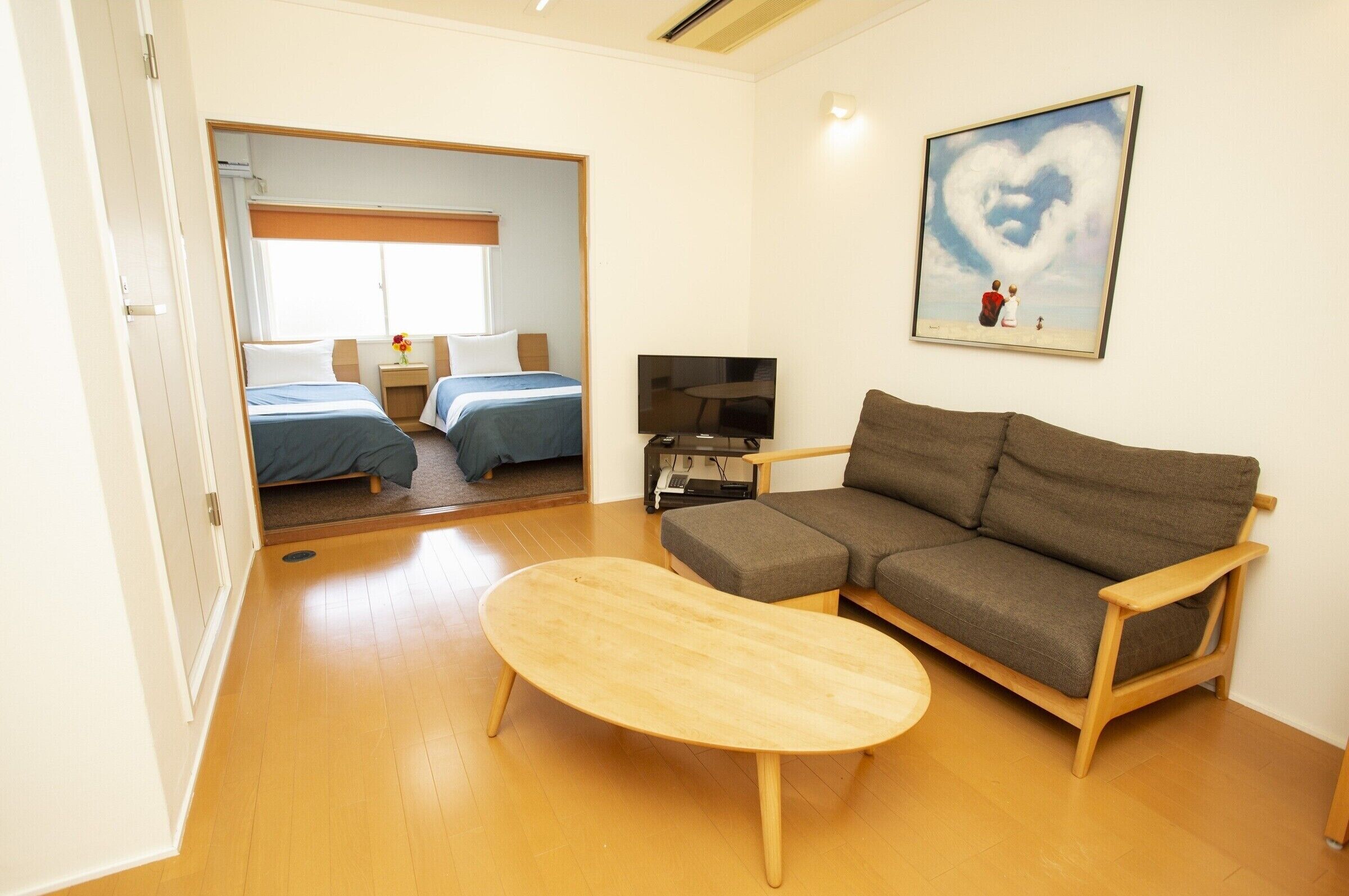 Una habitación con un sofá, una televisión, una cama con dos almohadas y un cuadro de un corazón en la pared.