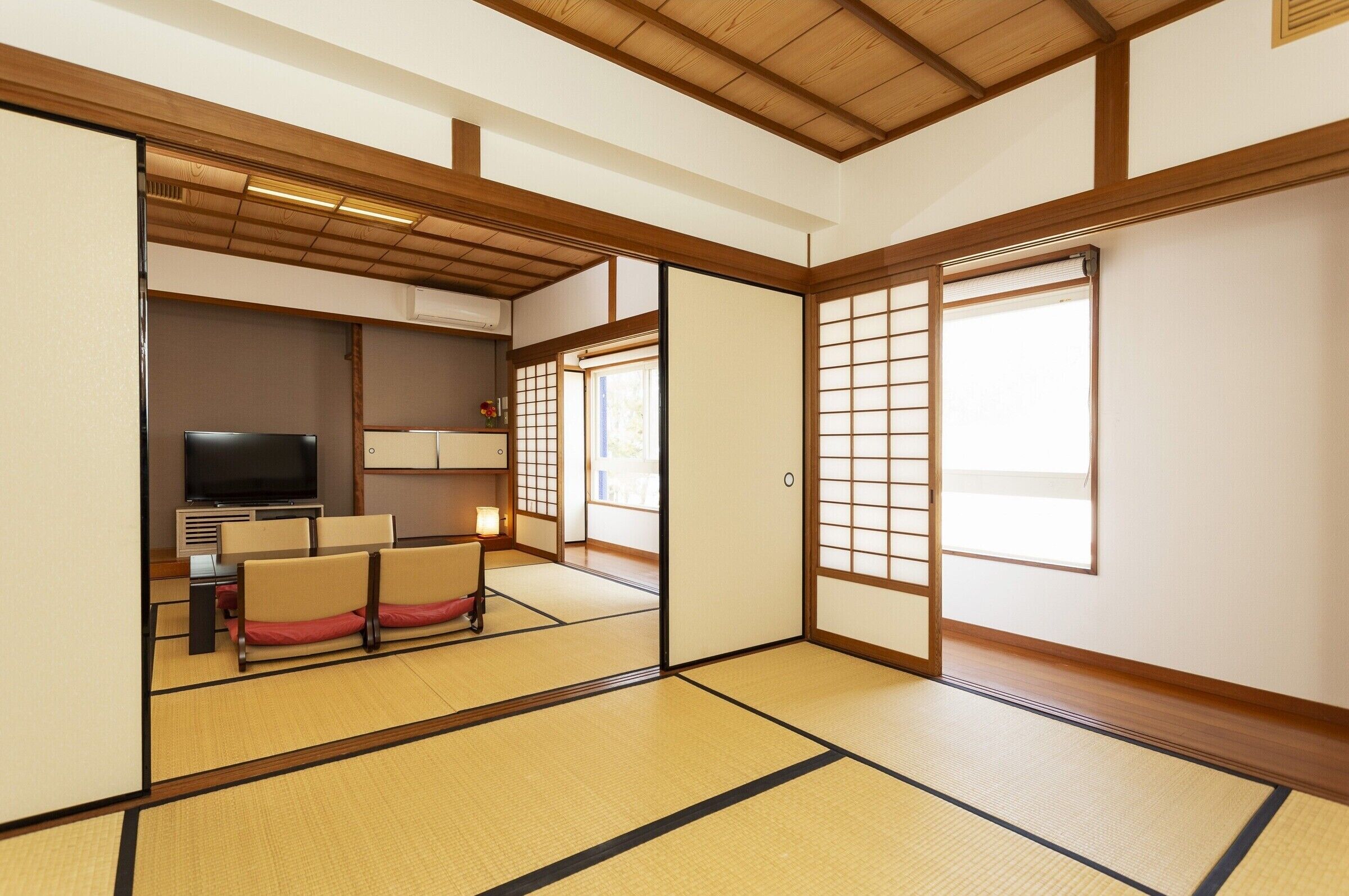 Ett traditionellt japanskt rum med tatamimattor på golvet, en tv, en soffa och skjutdörrar.