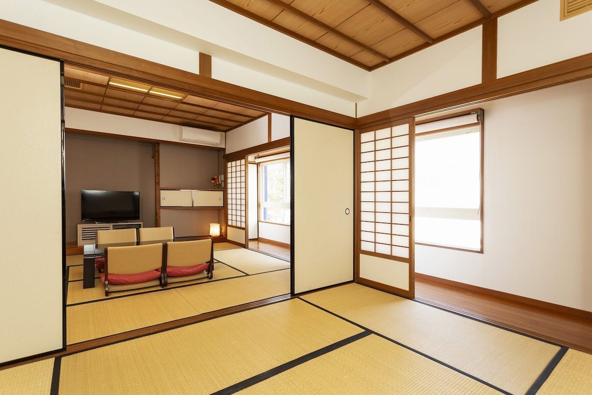 Ett traditionellt japanskt rum med tatamimattor på golvet, en tv, en soffa och skjutdörrar.
