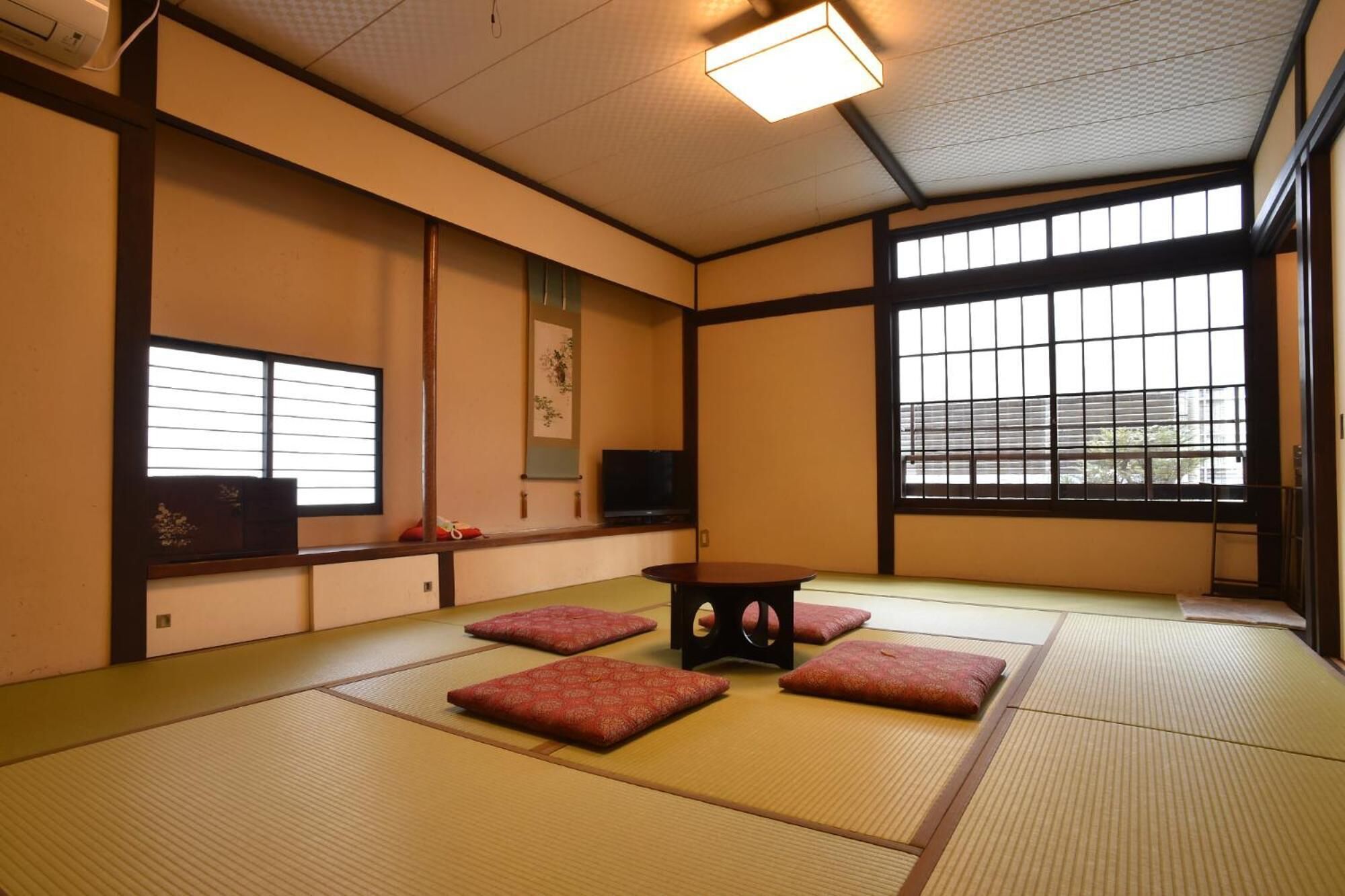 Une pièce avec un sol recouvert de tatamis, une table basse en tatami, des coussins, un téléviseur et une fenêtre donnant sur un paysage agréable.