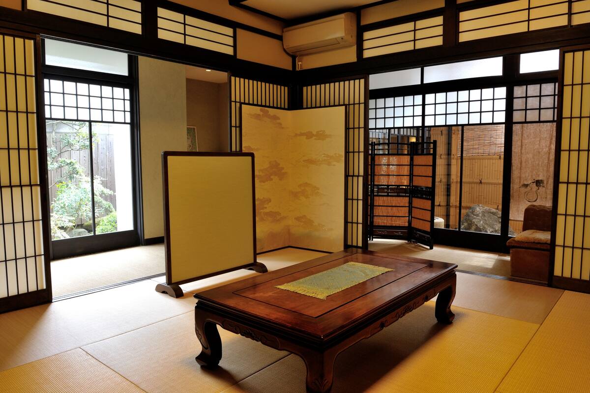 Une pièce de style japonais traditionnel, avec un sol recouvert de tatamis, une table en bois, des portes coulissantes et une vue sur un jardin.