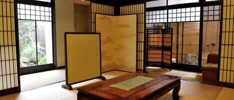 A traditional Japanese room with tatami flooring, a wooden table, sliding doors, and a view of a garden.