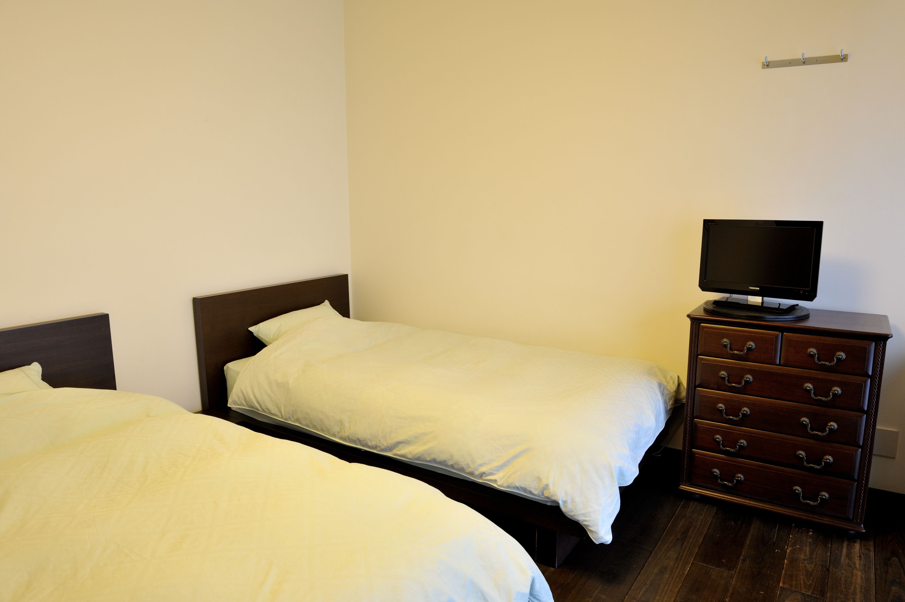 A room with two single beds, a wooden dresser with drawers, and a flat-screen TV on top.