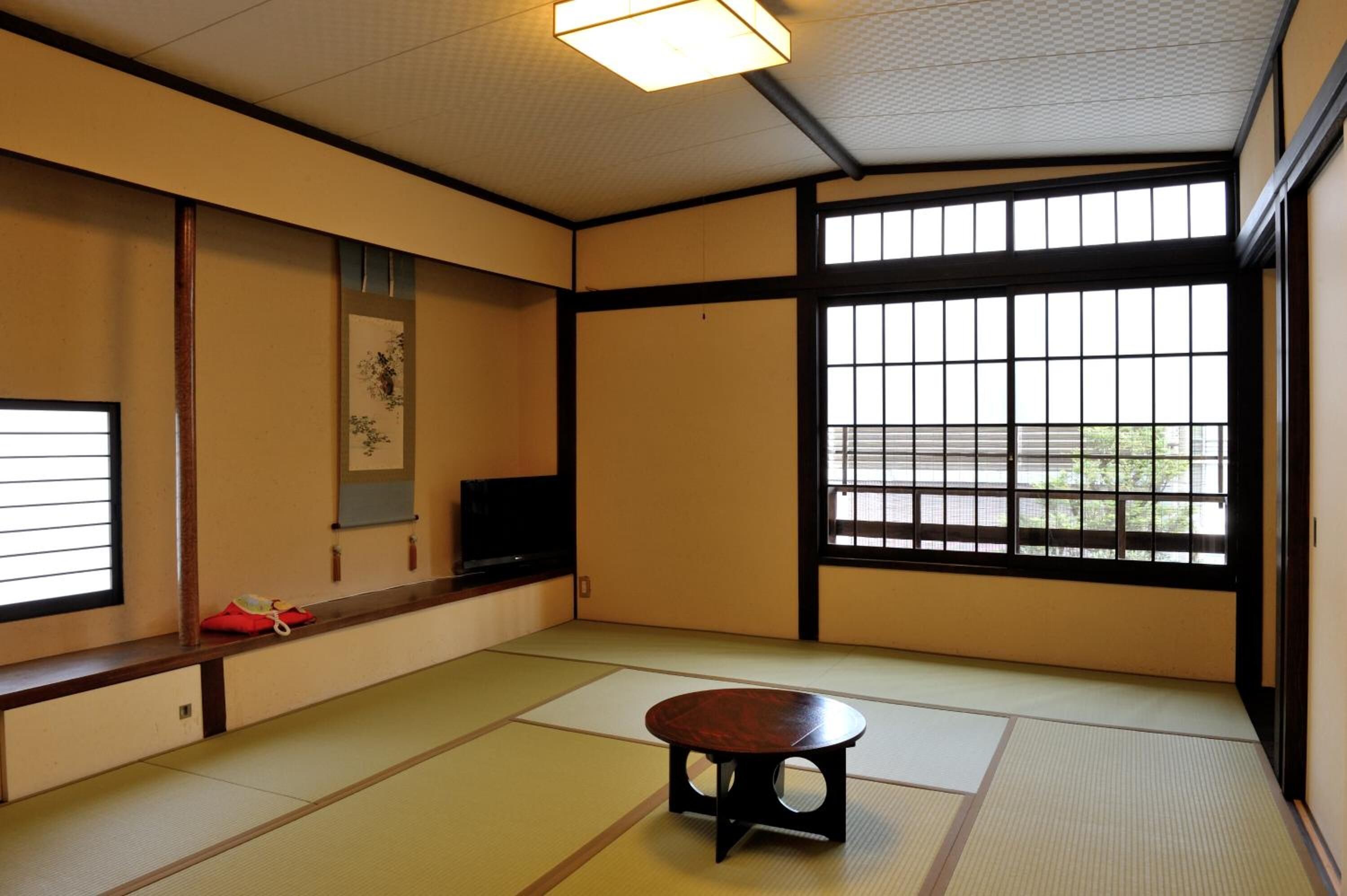 Una habitación japonesa tradicional con suelo de tatami, puertas correderas, televisor y una pequeña mesa.