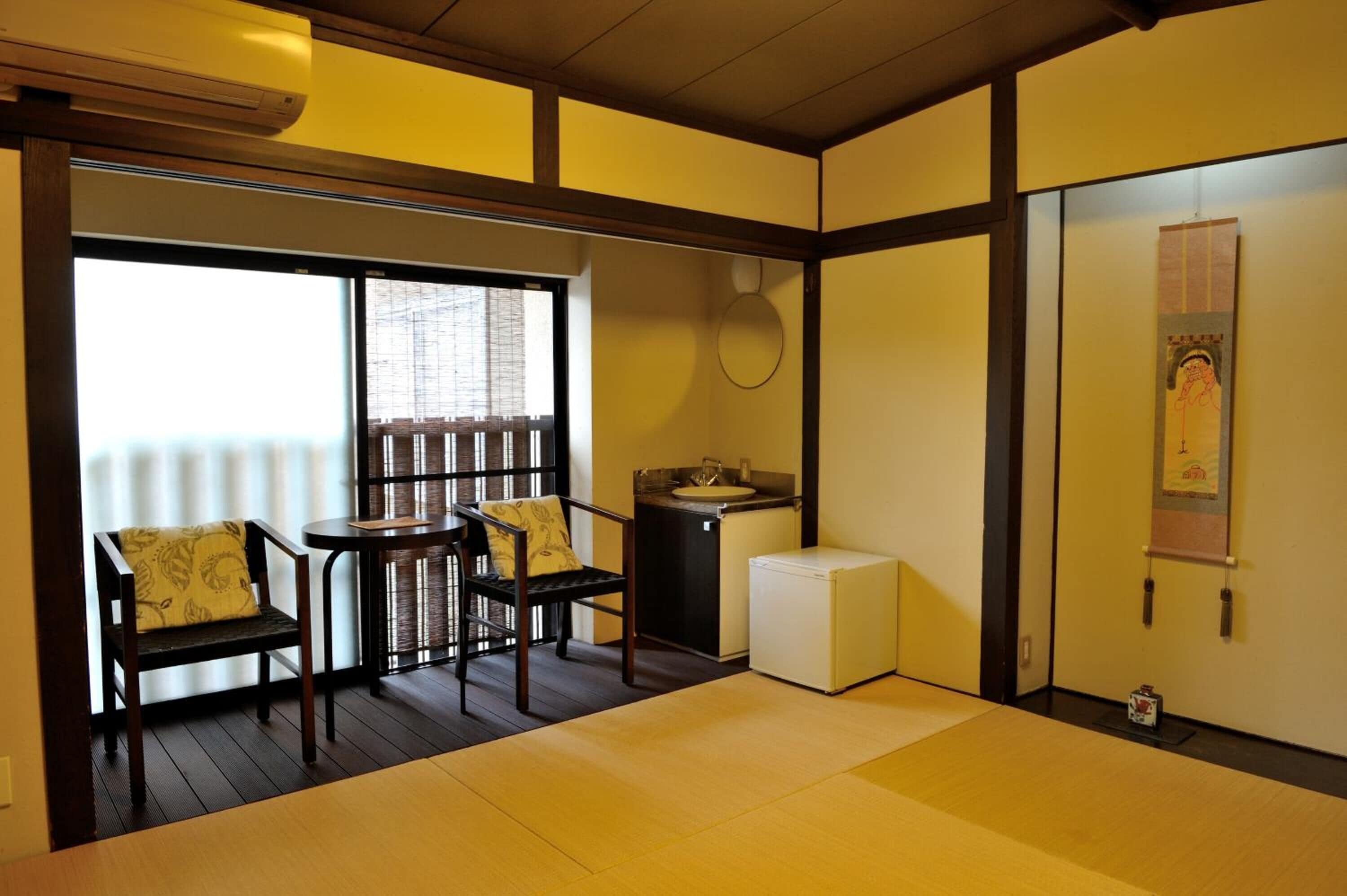 A traditional Japanese room with tatami flooring, a small table, two chairs, a sink, and a refrigerator.