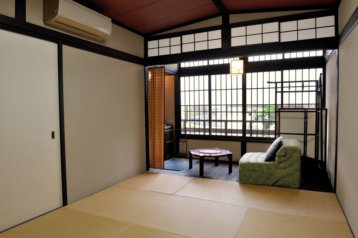 Une pièce de style japonais traditionnel, avec un sol recouvert de tatamis, une table basse, un canapé vert et une porte coulissante donnant sur un jardin.