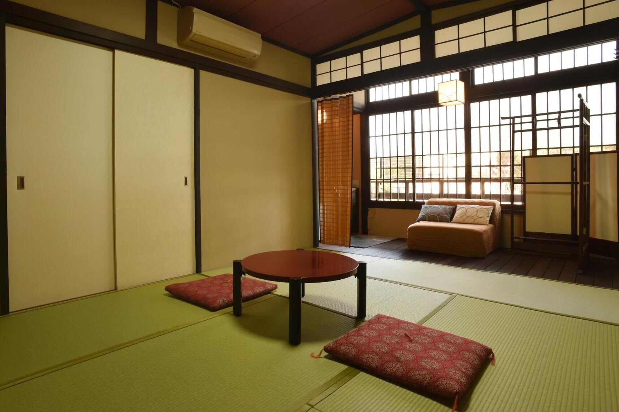 A traditional Japanese room with tatami flooring, a low table, cushions, and sliding doors.