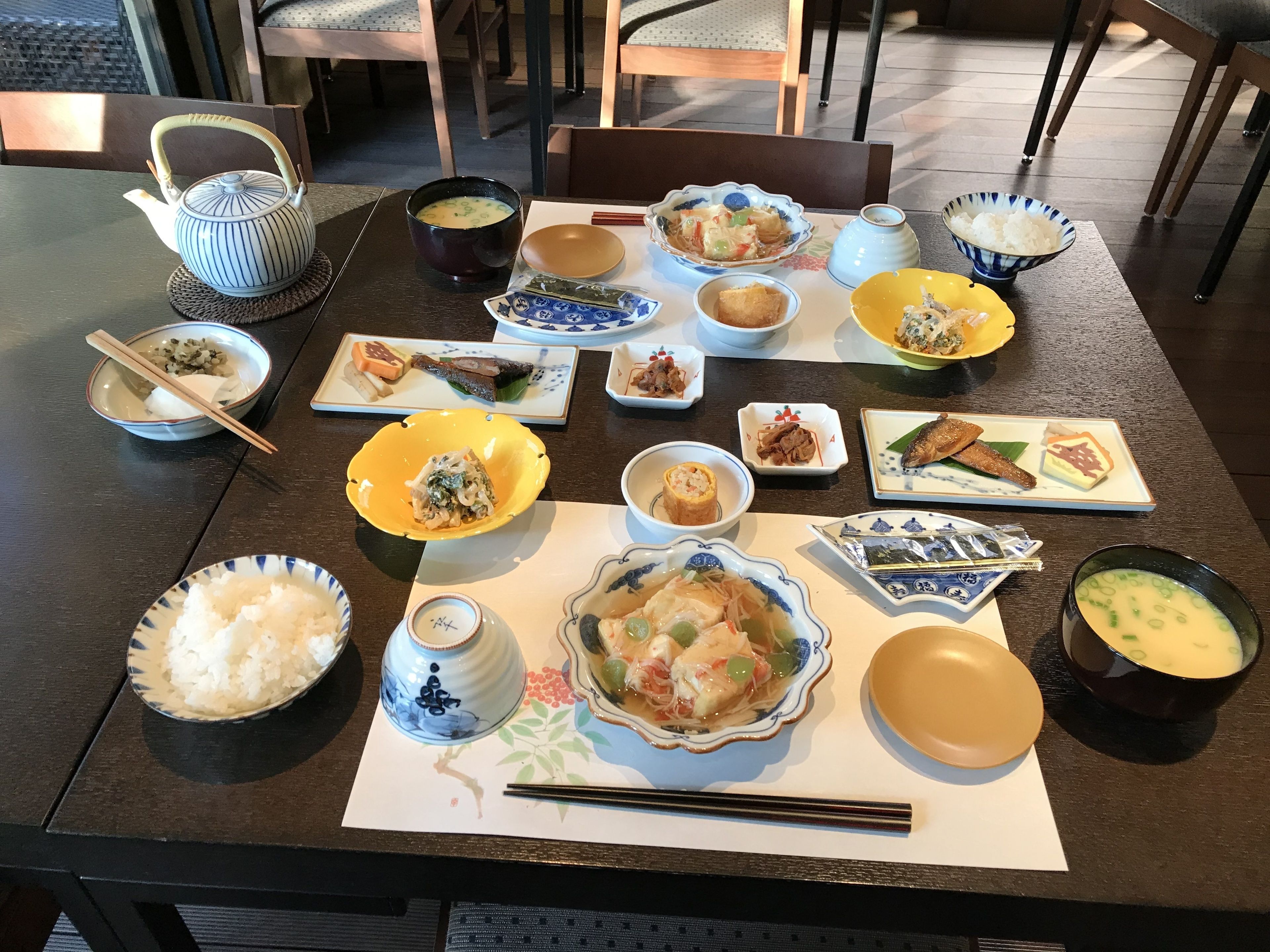 A dining table with various dishes, including bowls of soup, plates of food, and a teapot.