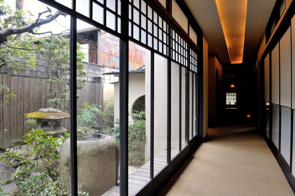 A corridor with tatami mat flooring, wooden walls, and a view of a garden with a stone lantern and a tree. - Yadoya Nishijinso (Kyoto)