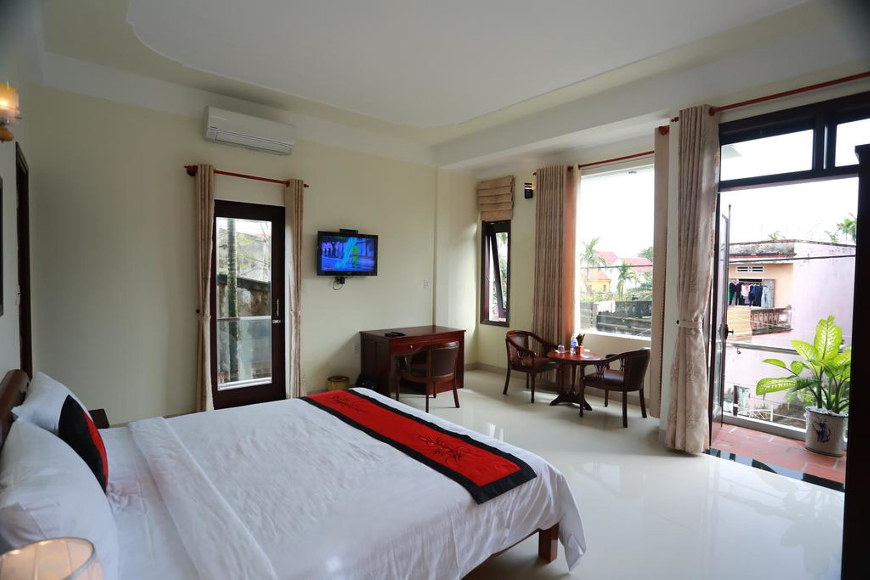 A hotel room with a bed, a desk, a chair, a TV, and a balcony with a view.