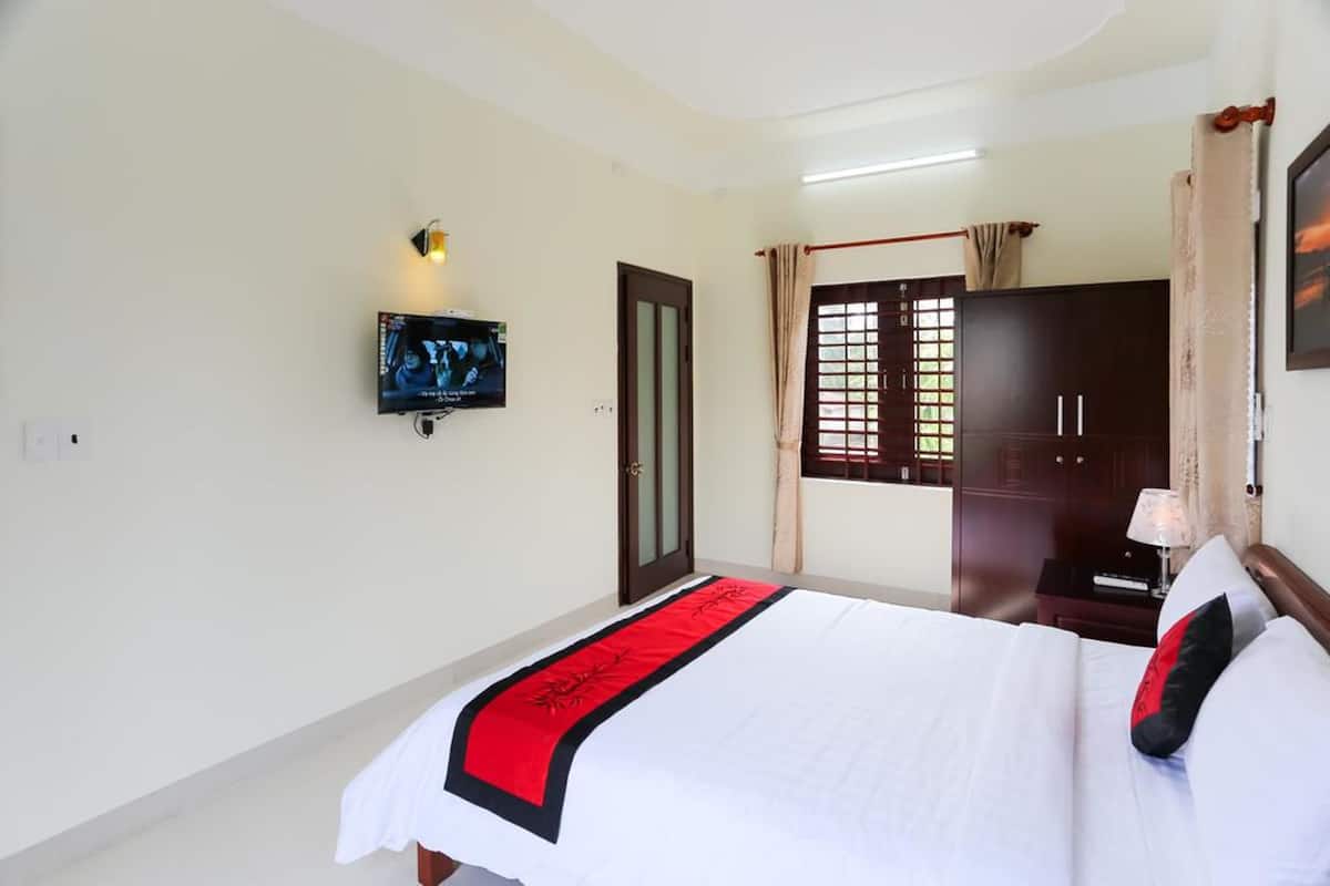 Una habitación de hotel con cama, televisión, armario y ventana con cortinas.