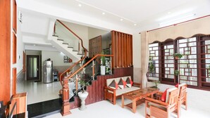 A spacious living area with a wooden staircase, a sofa set, and a dining table. - Viet Nhat Homestay (Da Nang)