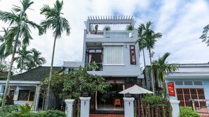 A two-story house with a balcony, surrounded by palm trees and a brick entrance. - Viet Nhat Homestay (Da Nang)